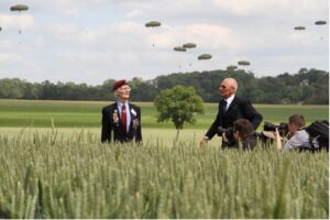 deux hommes dans un champs, présence de photographe et parachutiste en arrière-plan - commémoration du D-Day / crédit studios numériques